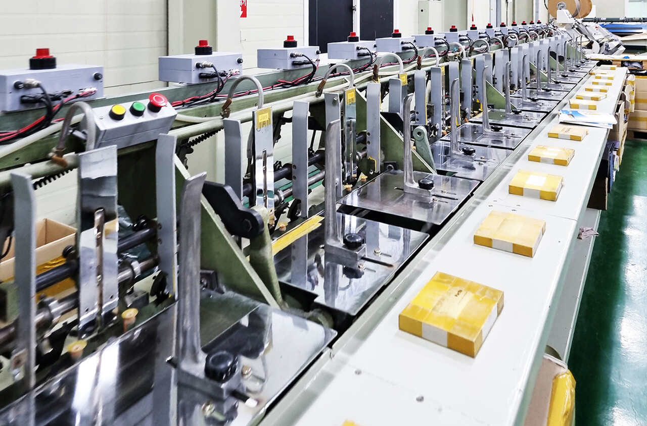 한국문구공업협동조합은 중소기업중앙회와 협력해 KC 유효기간 폐지와 환경표지 인증기준 개선을 이끌어내며 문구업계의 부담을 완화하고 경쟁력 강화를 뒷받침하고 있다. 한국문구공업협동조합 조합원사 공장에서 다이어리 제품의 자동 제본 및 포장 공정이 진행되는 모습.	[한국문구공업협동조합]